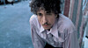 Bob Dylan i lys skjorte foran en blå væg.