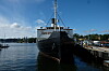Large cargo ship docked beside a pier on calm water with buildings in the distance.