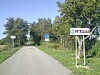 A tree-lined rural road with a Petržalka direction sign on the right