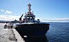 Remolcador negro atracado en un muelle de Punta Arenas, con mar abierto y cielo despejado al fondo.